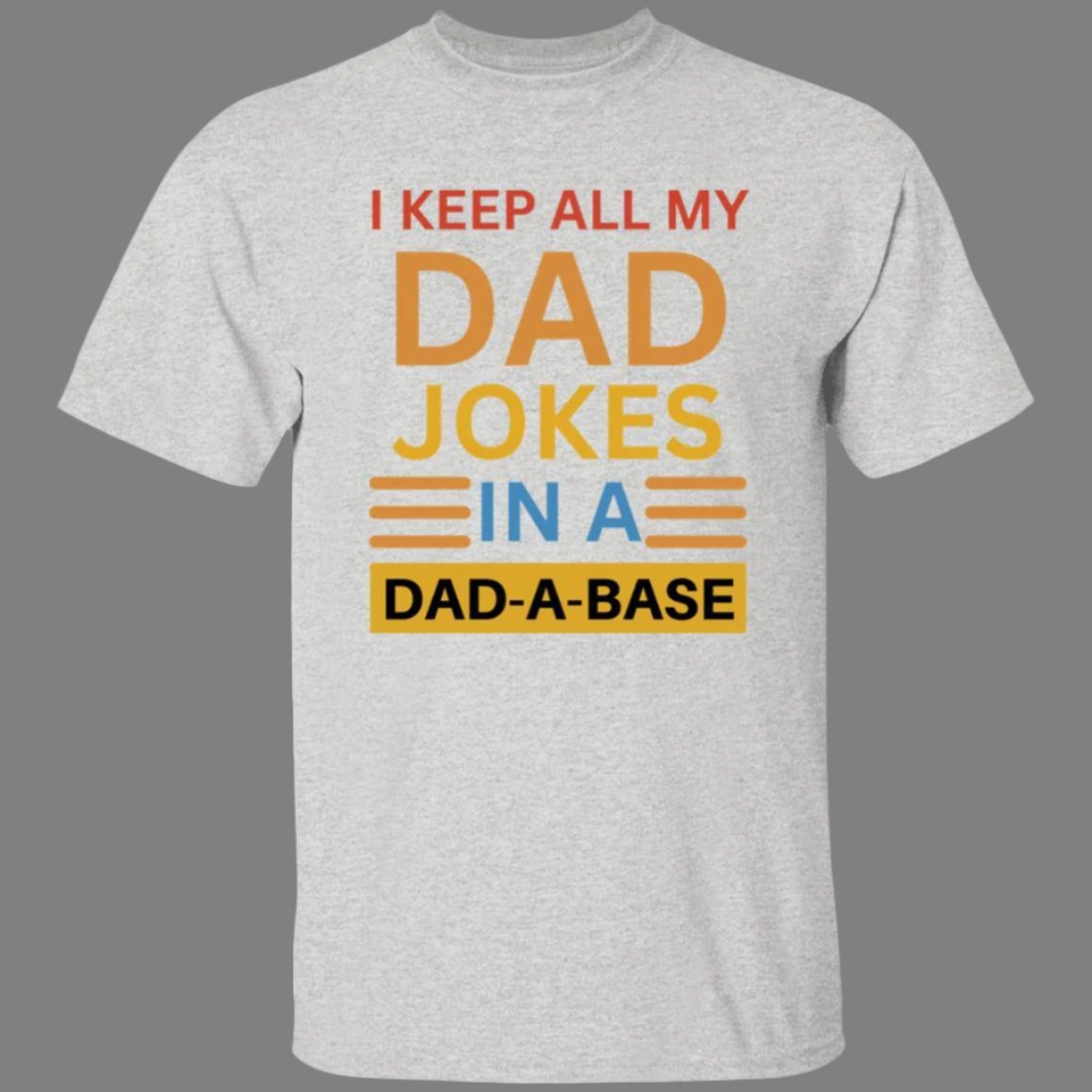 Ash gray, heavyweight classic unisex t-shirt in 100% cotton. On the front is printed: I keep all my DAD jokes in a DAD-A-BASE - Any Gift For You